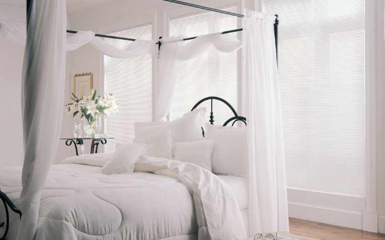 airy white sheer curtains in all-white bedroom with canopy bed